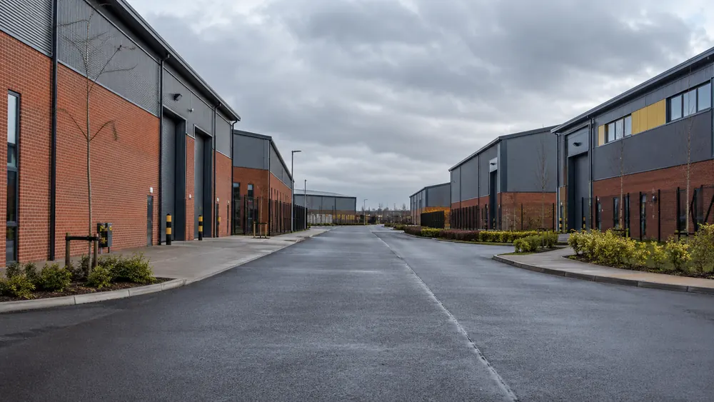 Red brick industrial buildings and a modern warehouse beside a quiet commercial access road